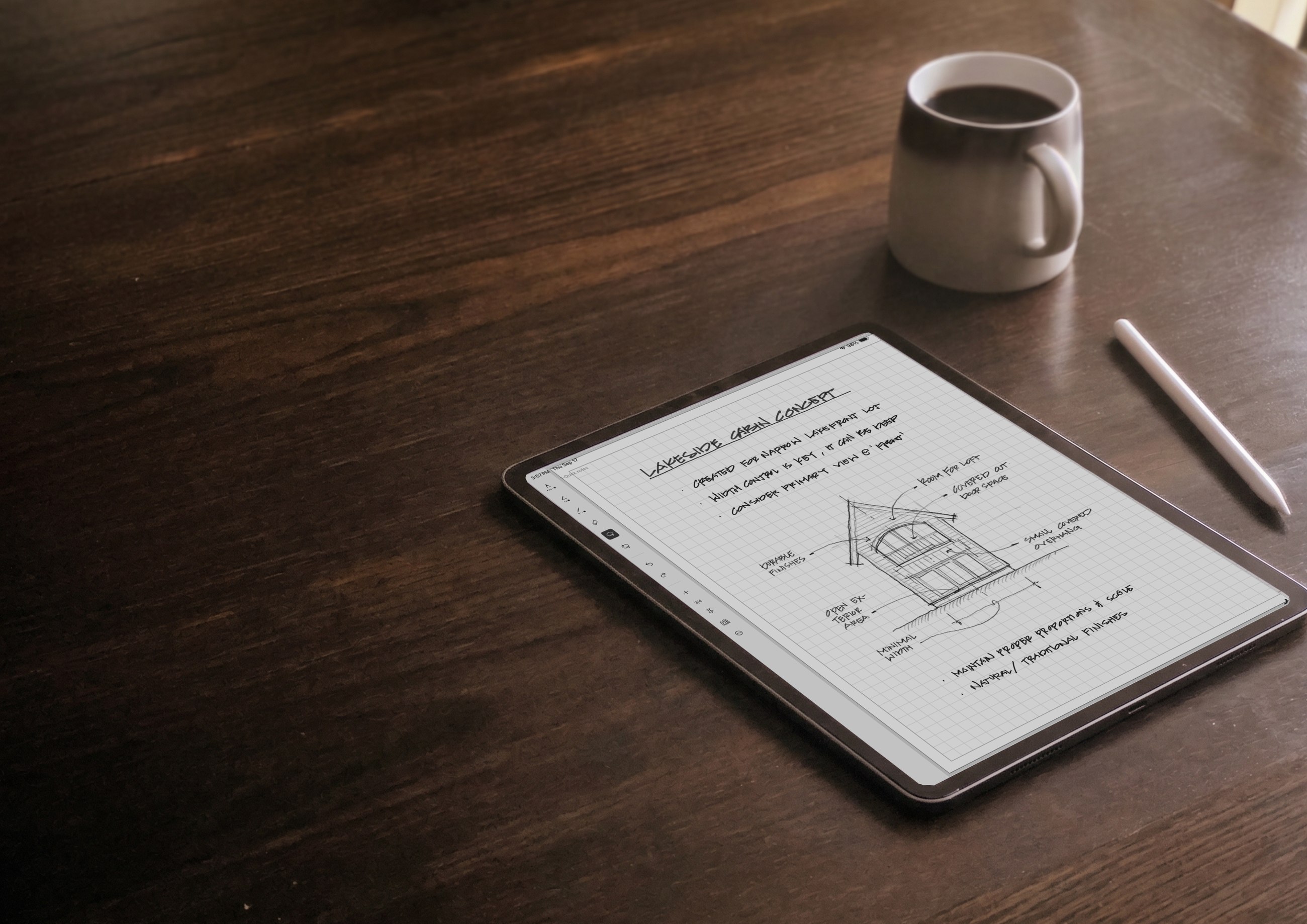 An iPad and Apple Pencil resting on a wooden table, showing a handwritten cabin design sketch.